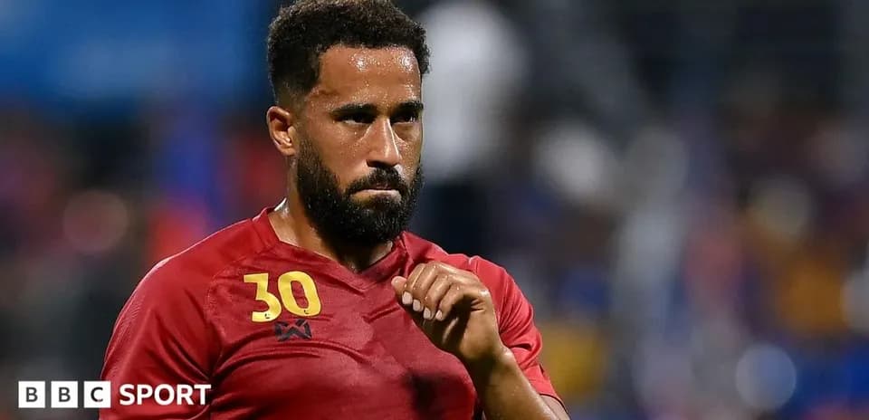 Joueur en maillot rouge, regard sérieux sur le terrain