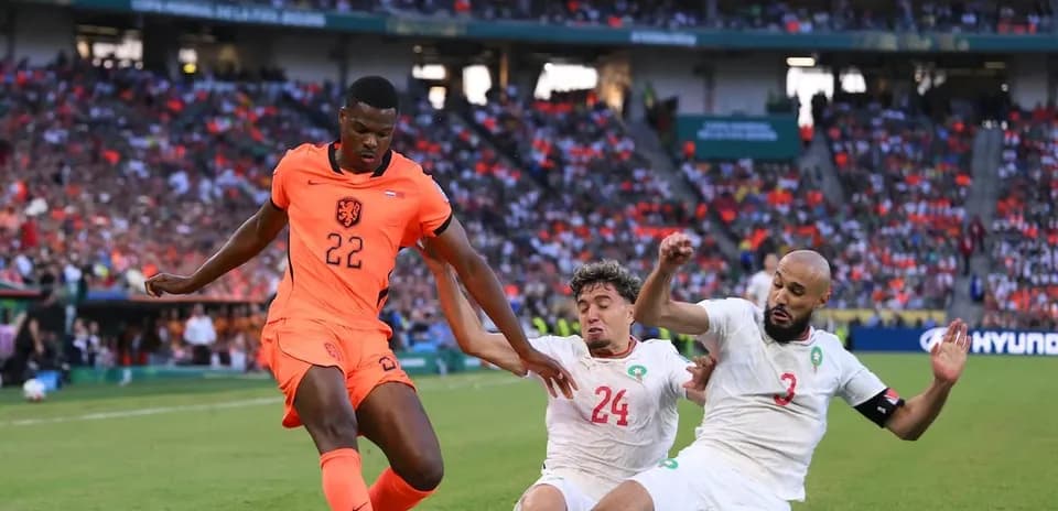 Joueur néerlandais dribblant entre deux défenseurs marocains