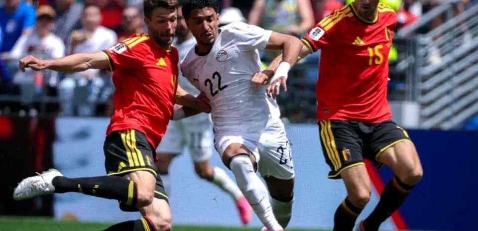 Joueur égyptien dribblant entre deux défenseurs belges