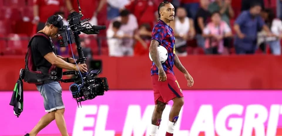 Joueur avec un ballon sur le terrain, cameraman à proximité