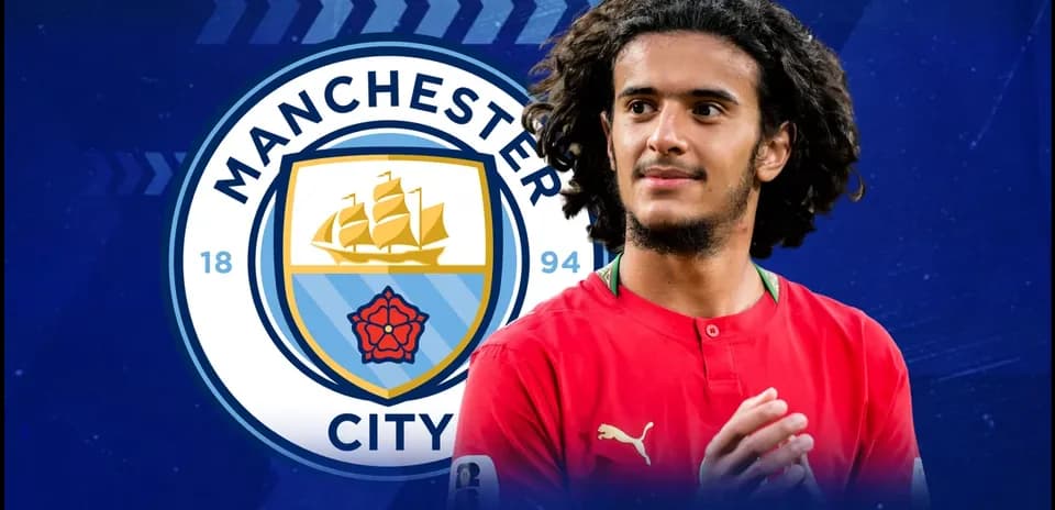 Joueur avec maillot rouge devant le logo de Manchester City