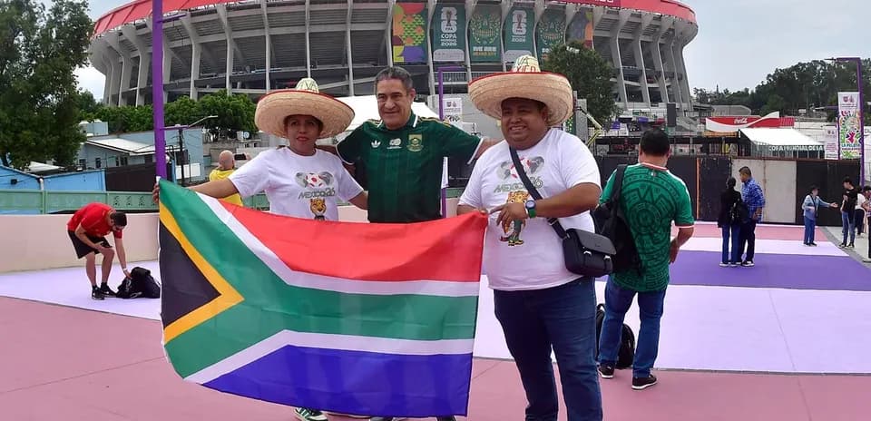 Trois supporters avec un drapeau sud-africain devant le stade