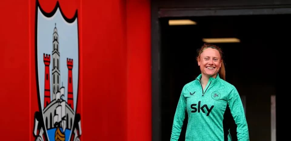 Joueuse souriante portant un maillot vert à l'entrée du stade