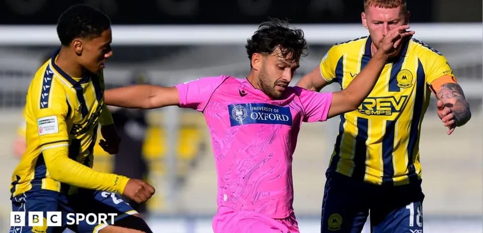 Joueur en rose dribblant entre deux adversaires en bleu