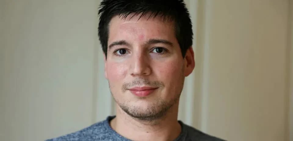 Homme souriant avec un t-shirt gris devant un mur
