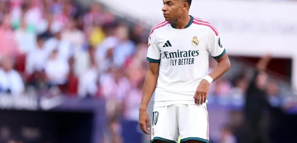 Kylian Mbappé debout sur le terrain avec des supporters en arrière-plan