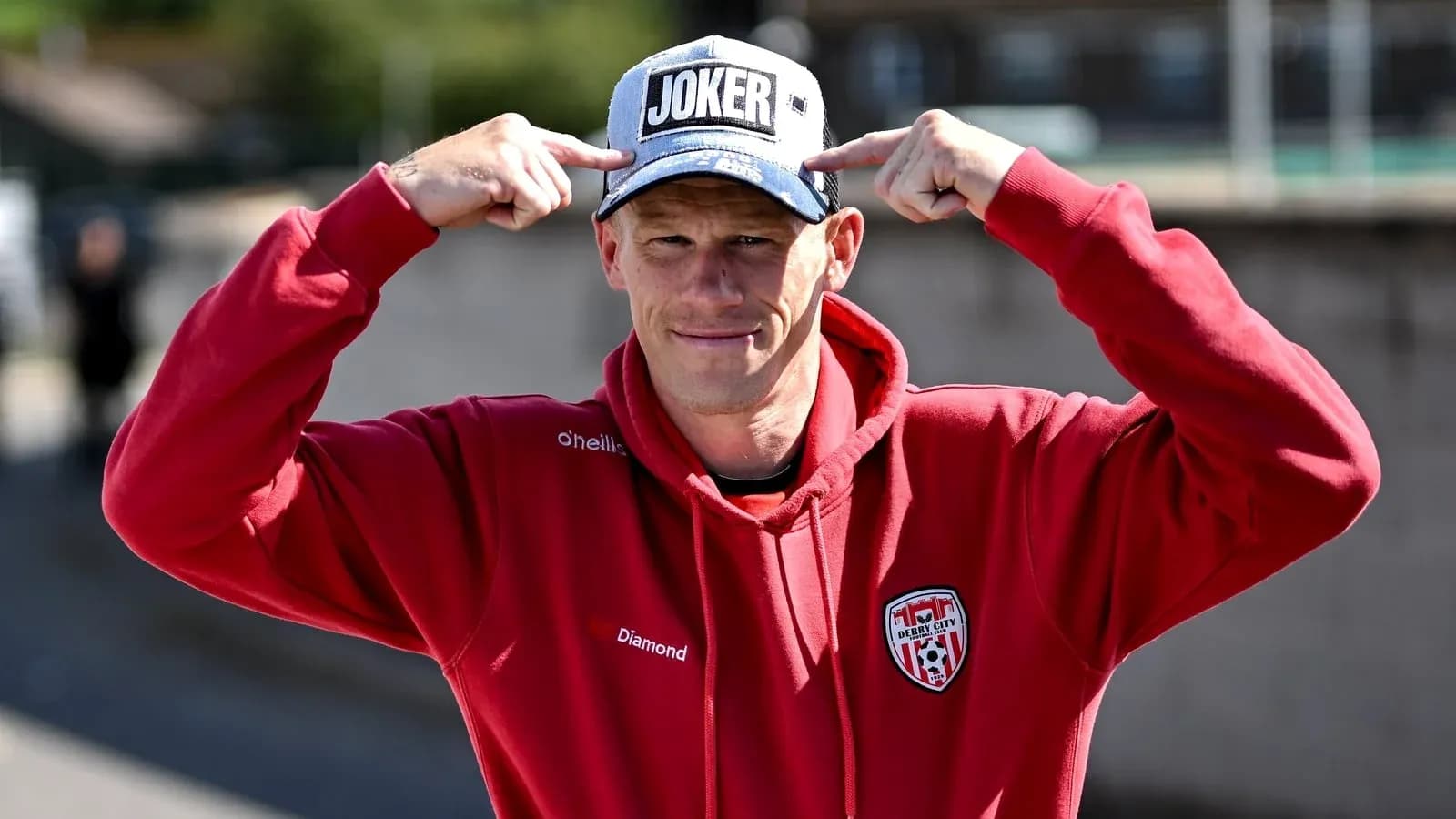 Homme en sweat rouge portant une casquette 'JOKER' Homme en sweat rouge portant une casquette 'JOKER'
