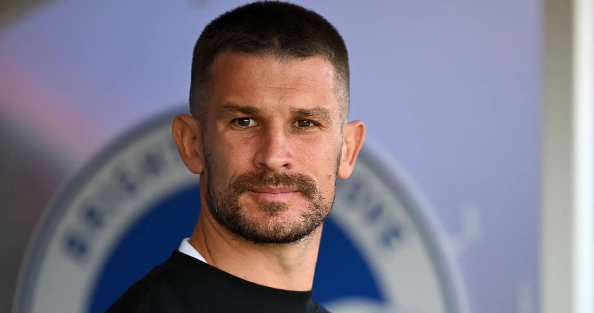 Joueur avec barbe posant près du logo de l'équipe Joueur avec barbe posant près du logo de l'équipe