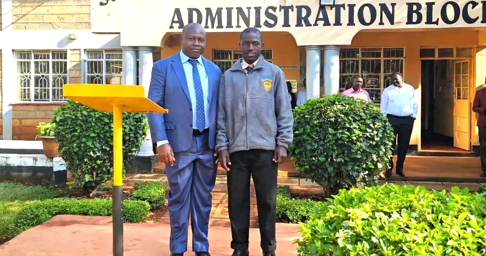 Deux hommes posant devant le bloc administratif d'une école Deux hommes posant devant le bloc administratif d'une école